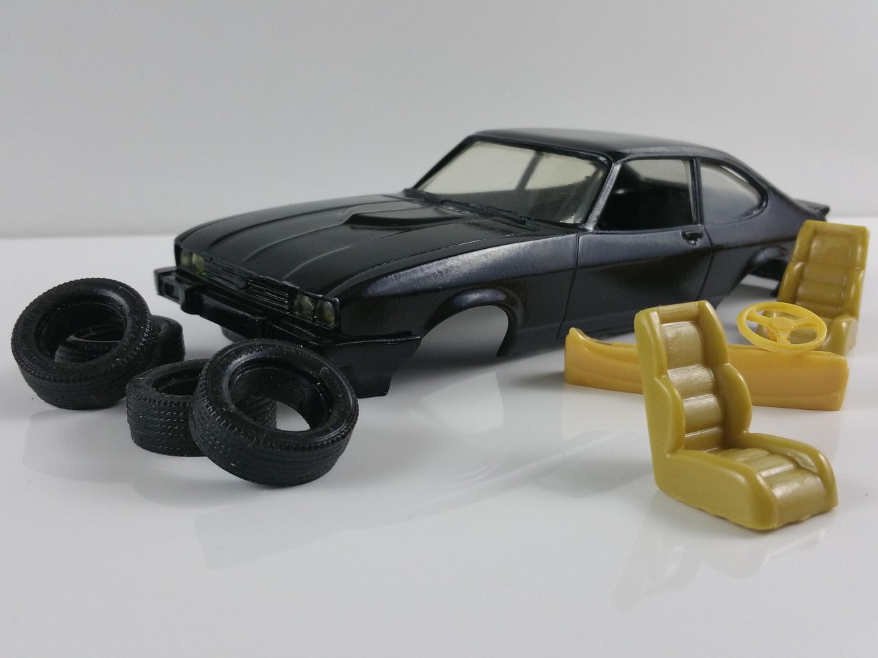 1/24 scale Ford Capri model kit in gloss black with unassembled parts, including rubber tires and yellow interior components, showcasing detailed body casting and authentic muscle car styling